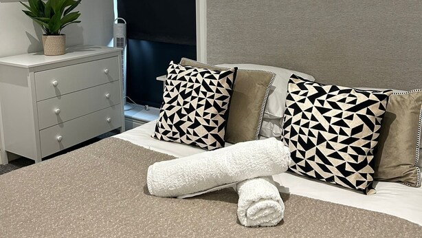 Un dormitorio moderno con cama, cómoda, planta en maceta y una ventana grande.