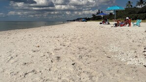 En strand med fodaftryk i sandet, en klar himmel og et par strandparasoller.