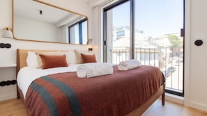 Une chambre d’hôtel avec un grand lit, un miroir, une fenêtre et une vue sur les immeubles.