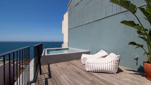 Terraza en la azotea con jacuzzi, cojines a rayas y una planta en maceta.