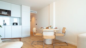 Una cocina moderna con armarios blancos y un microondas Bosch. Hay una mesa de comedor redonda con cuatro sillas de mimbre y una mesita auxiliar.