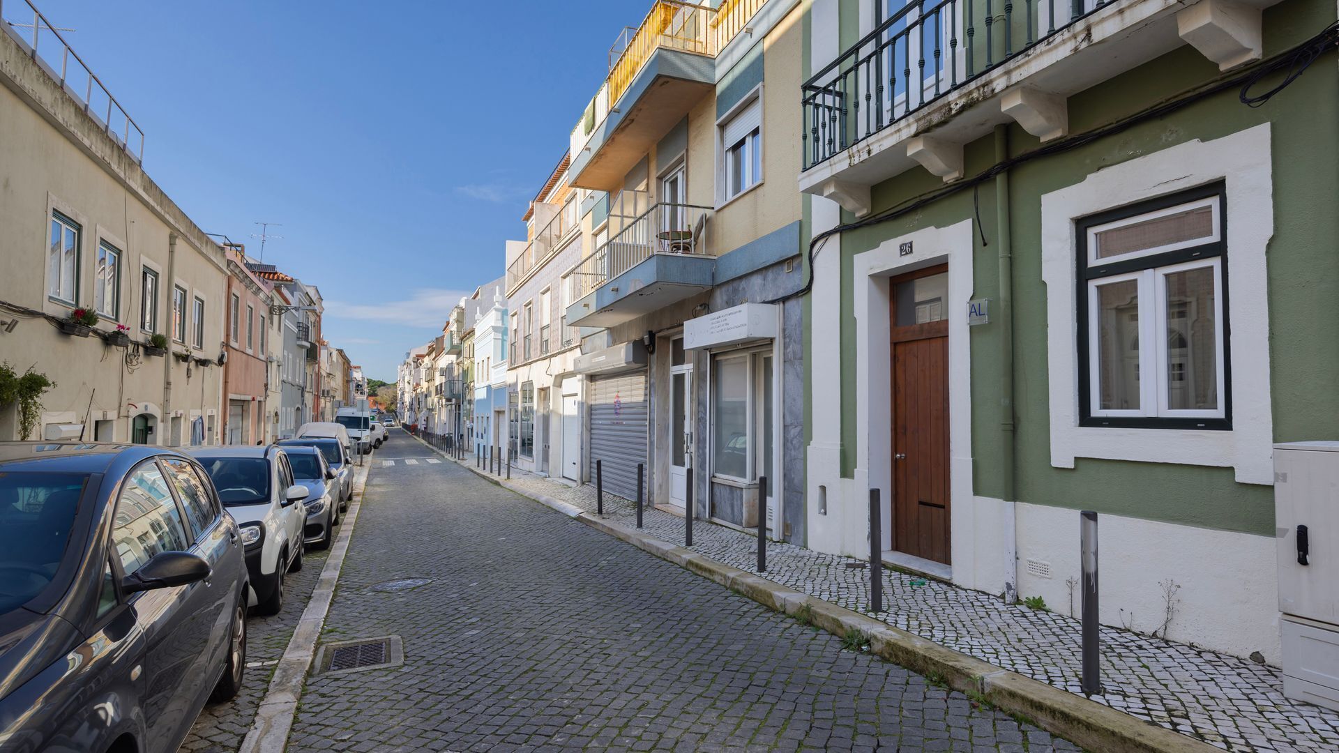 Une ruelle étroite pavée, bordée d’immeubles à plusieurs étages, dont certains sont dotés de balcons et d’autres de volets fermés.