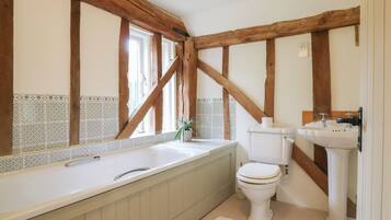 A bathroom with a bathtub, toilet, and sink, featuring exposed wooden beams and patterned tiles.