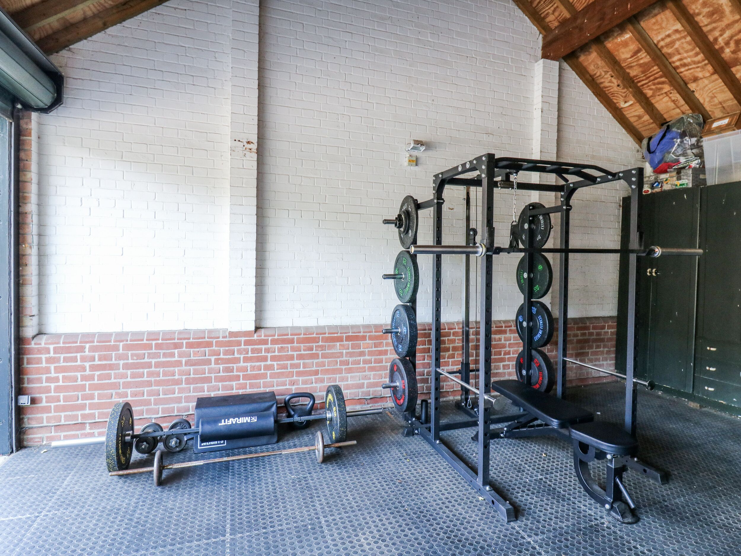 A gym with weightlifting equipment, a brick wall, and a wooden ceiling.