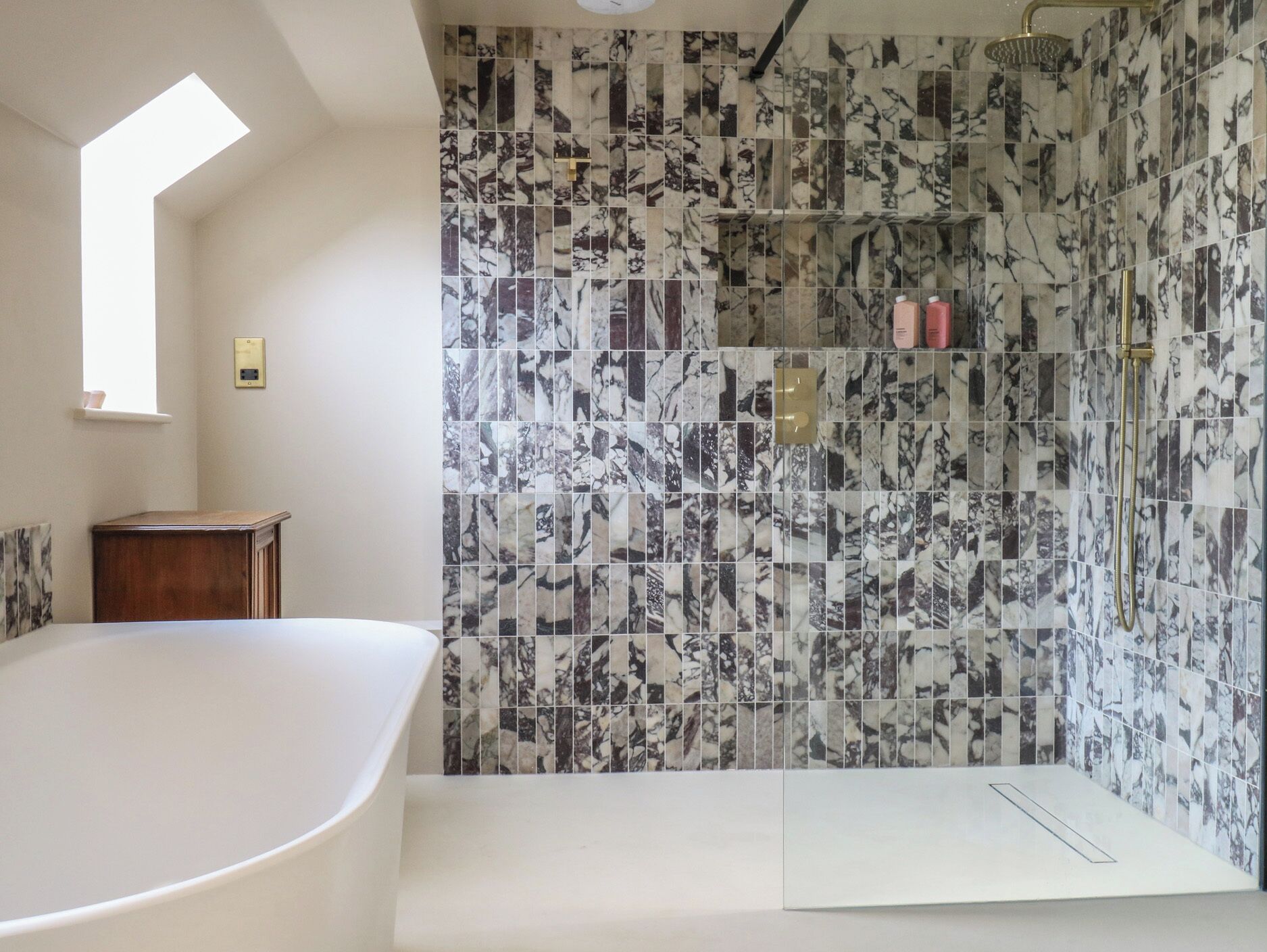 A bathroom with a freestanding bathtub, a shower with a gold showerhead, and a tiled wall with a marble pattern.