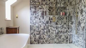 A bathroom with a freestanding bathtub, a shower with a gold showerhead, and a tiled wall with a marble pattern.