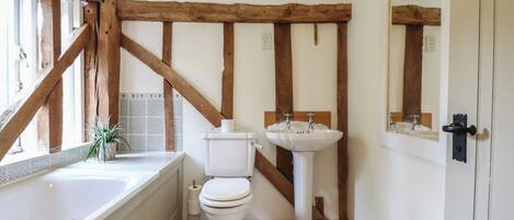 A bathroom with a bathtub, toilet, and sink, featuring exposed wooden beams and a tiled backsplash.