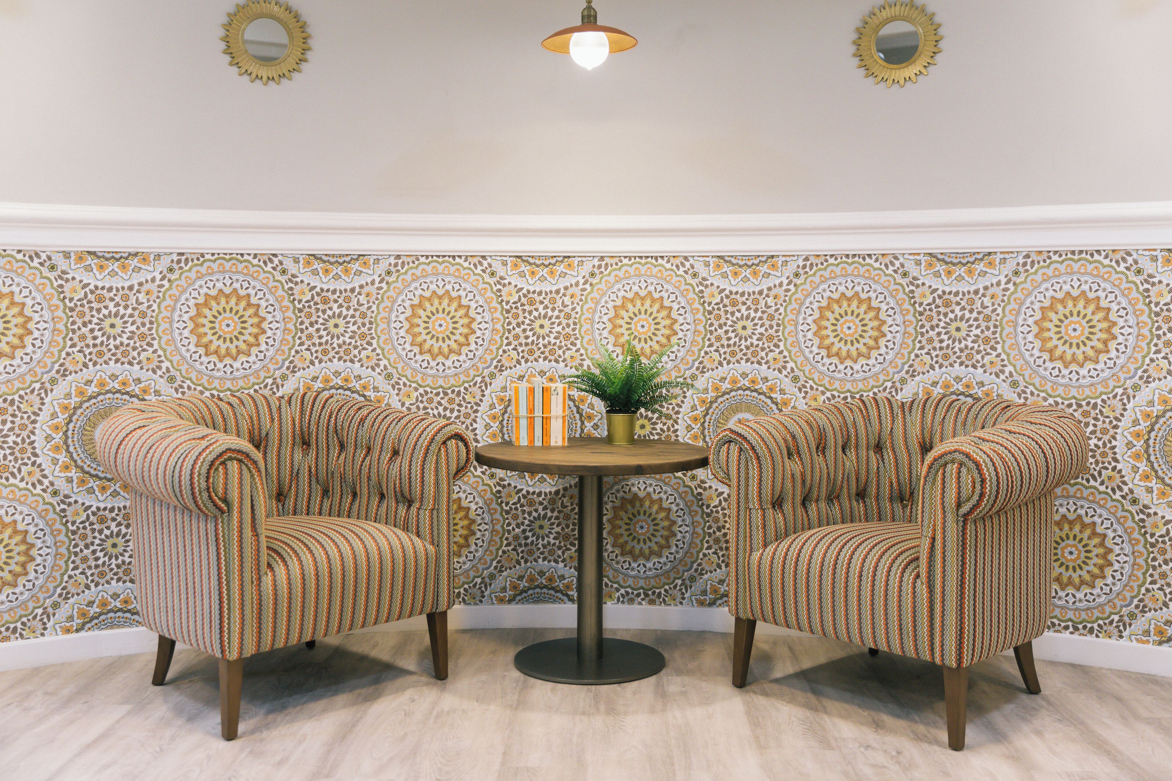 Une pièce comprenant deux fauteuils rembourrés, une petite table ronde et un mur orné d’un motif.