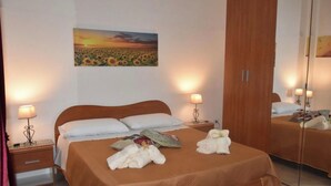 A hotel room with a bed, bedside lamps, a mirror, a painting of a sunset over a field, and a wardrobe. - Vacation House Giorgia (Marinella)