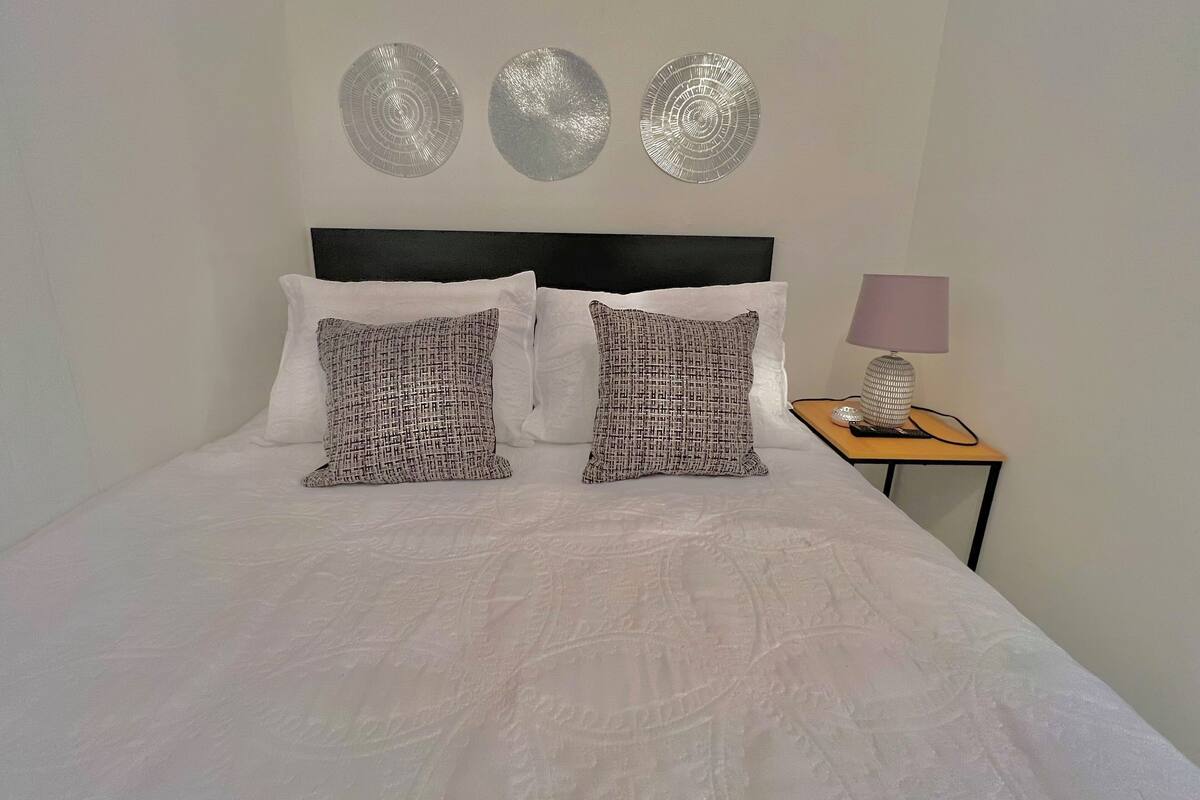A neatly made bed with patterned pillows, a black headboard, and a bedside table with a lamp and decorative item.