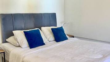 Ein Bett mit grauem Kopfteil, weißer Bettwäsche und zwei blauen Kissen.