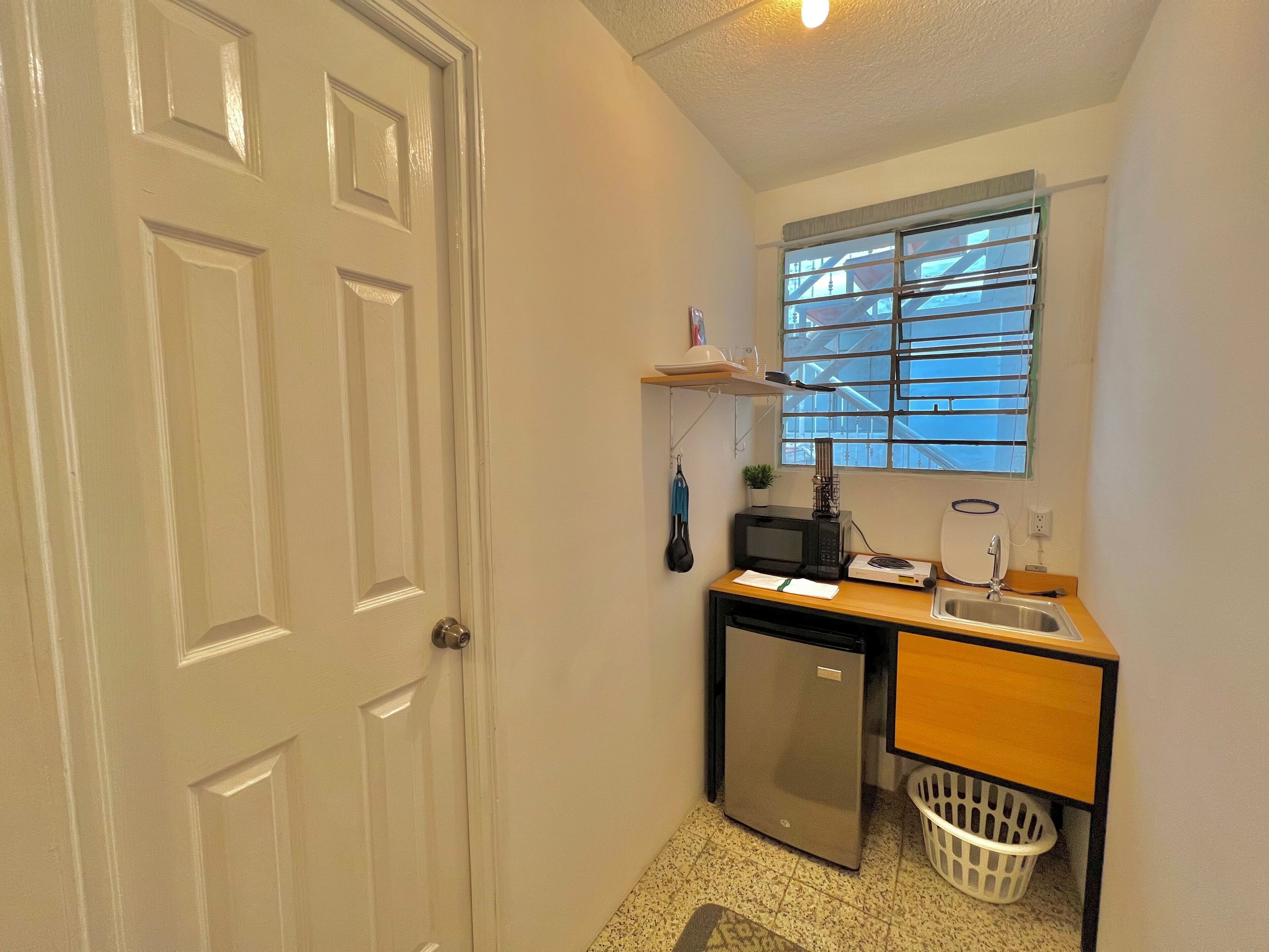Una kitchenette compacta con refrigerador, microondas y lavamanos.