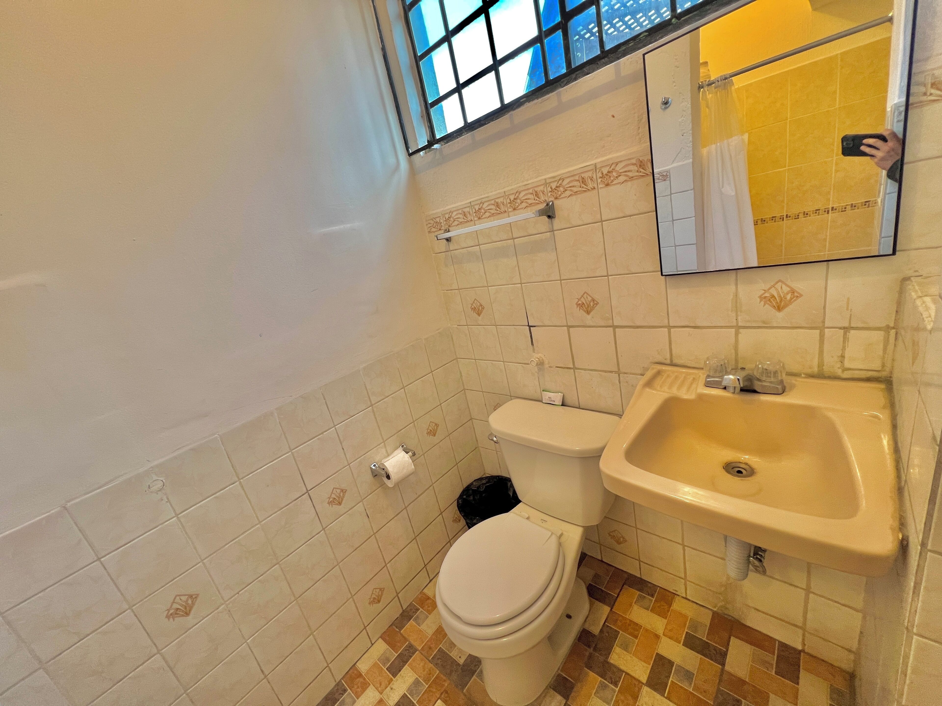 Egy fürdőszoba, amelyben WC, mosdókagyló és egy ablak található, melyből kilátás nyílik a külvilágra.