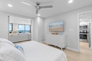Een moderne slaapkamer met een groot bed, een plafondventilator, een televisie op een dressoir en uitzicht op de oceaan.