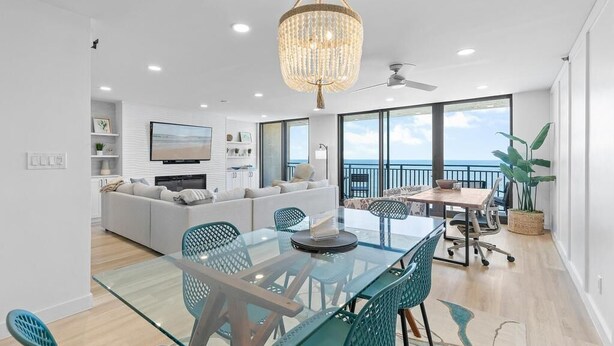 A modern living room with a glass dining table, teal chairs, a chandelier, and a sofa set. - Moontide B707 (New Smyrna Beach)