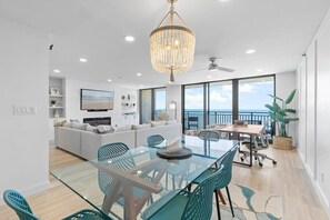 Un salon moderne avec une table à manger en verre, des chaises turquoise, un lustre et un ensemble de canapés.