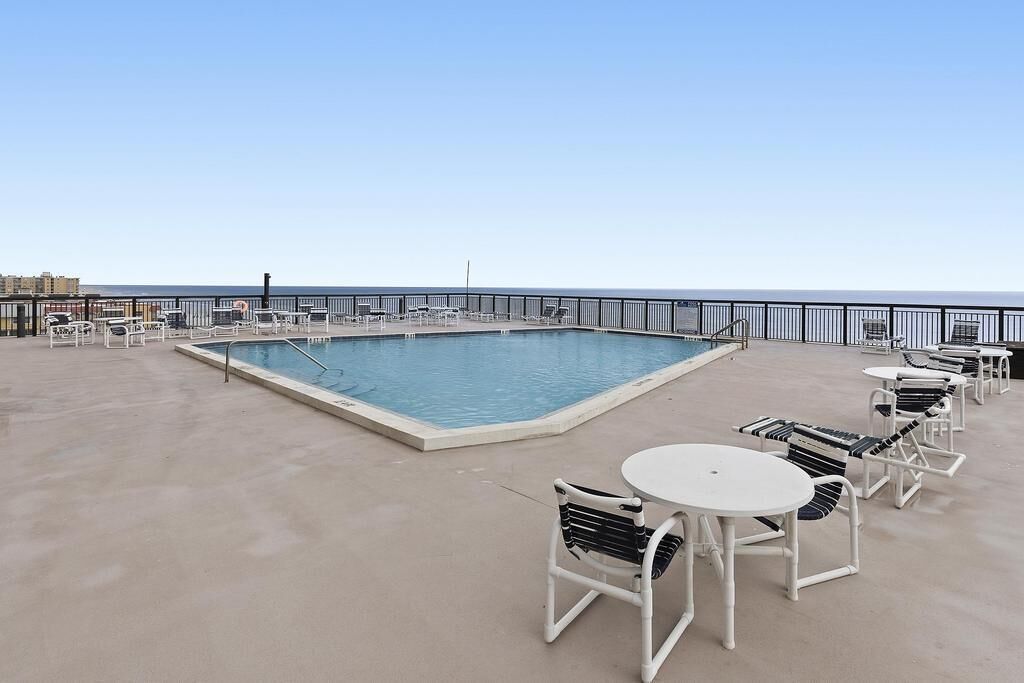 A rooftop pool area with a clear view of the ocean, surrounded by lounge chairs and tables.