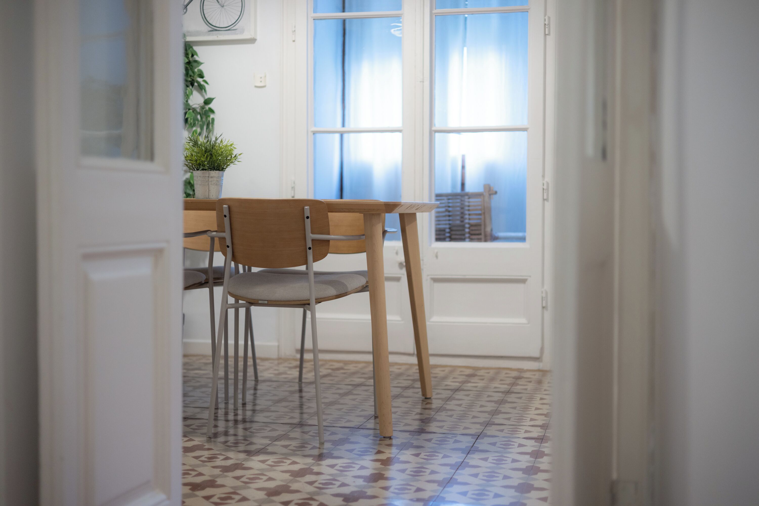 Ein Essbereich mit Holztisch und Stühlen, einem Blumentopf und einem Fenster mit Vorhängen.