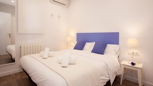 A hotel room with a large bed, white bedding, a blue headboard, bedside lamps, and an air conditioning unit. - Stay U-nique Apartments Sant Pau (Barcelona)