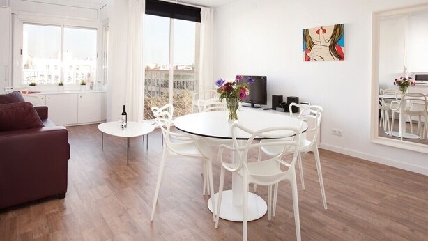 A modern living room with a dining area, large windows, and a city view. - Stay U-nique Apartments Sant Pau (Barcelona)