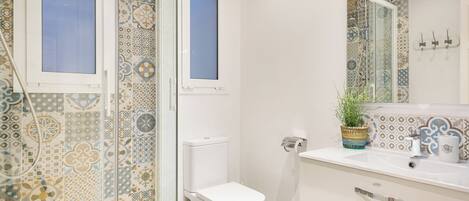 A bathroom with patterned tiles, a toilet, a shower with a glass door, and a sink with a mirror.