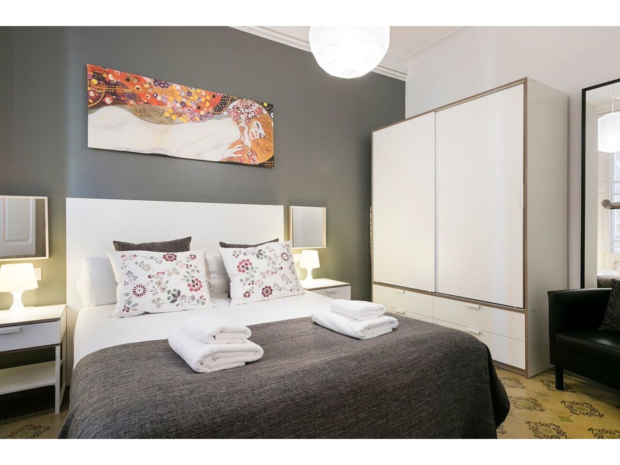 A modern hotel room with a large bed, a wardrobe, and a painting on the wall.