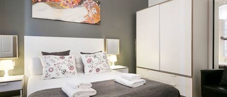 A modern hotel room with a large bed, a wardrobe, and a painting on the wall.