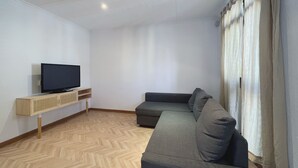 A modern living room with a flat-screen TV on a wooden stand, a grey sofa, and a herringbone-patterned wooden floor. - Stay U-nique Apartments Calabria (Barcelona)