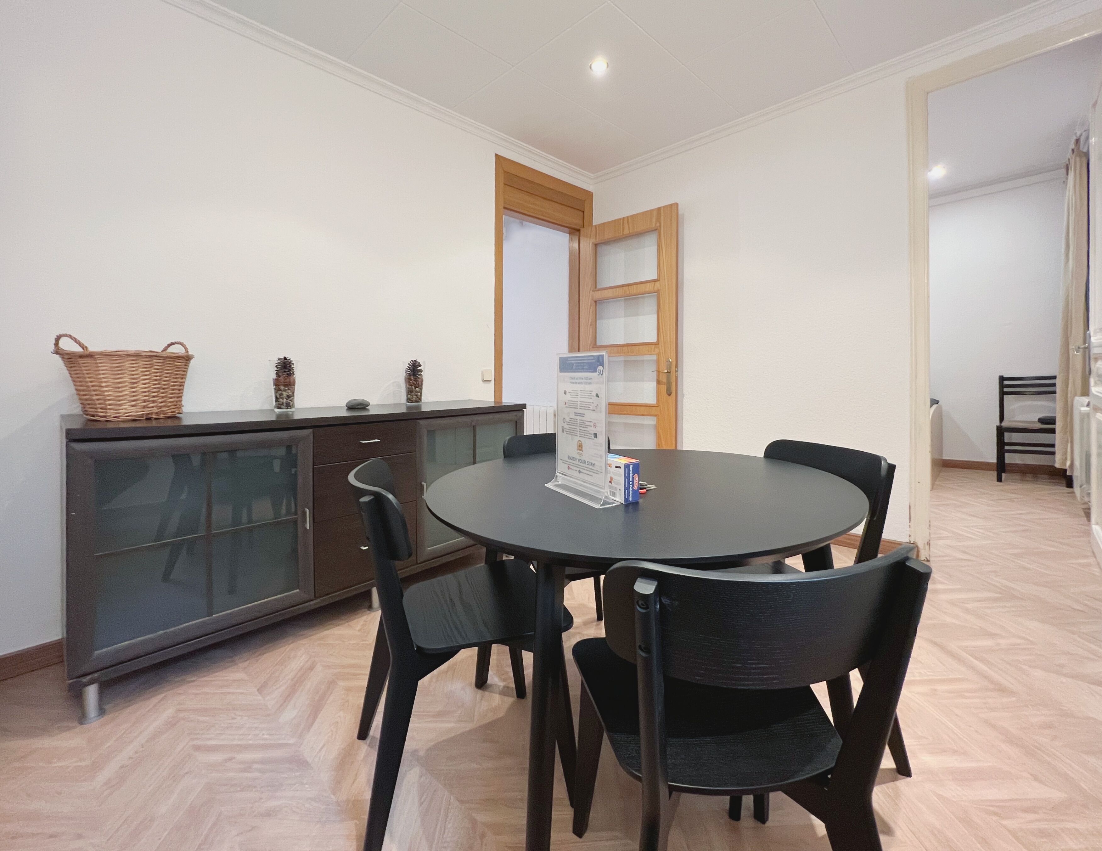 A dining area with a round table, four chairs, a cabinet with glass doors, and a basket on the cabinet.