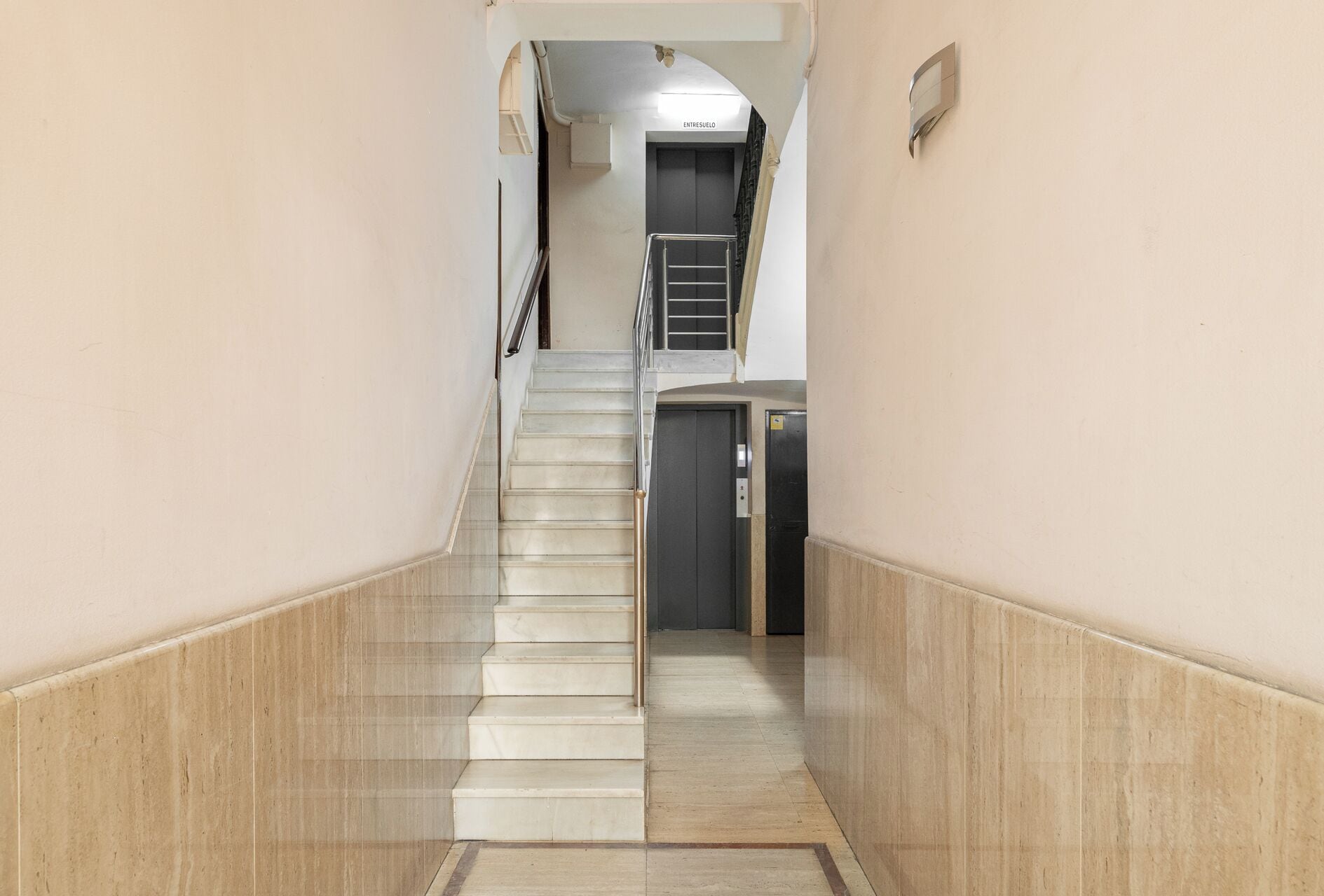 A corridor with a marble floor leading to a staircase and an elevator.