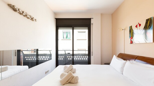 A hotel room with a bed, a desk, a mirror, and a window with a view of buildings. - Stay U-nique Apartments Bonsoms (Barcelona)