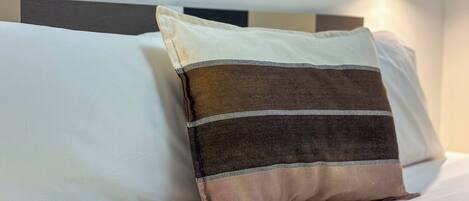 A bed with two pillows, one plain and one striped, in a room with a modern headboard and a wall-mounted light fixture.