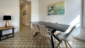 Un coin repas avec une table en verre, des chaises blanches, une lampe noire et un tableau représentant une vague japonaise accroché au mur.