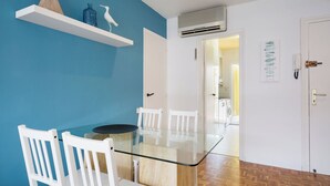 Una habitación con una mesa de vidrio, sillas blancas, pared azul y piso de madera.