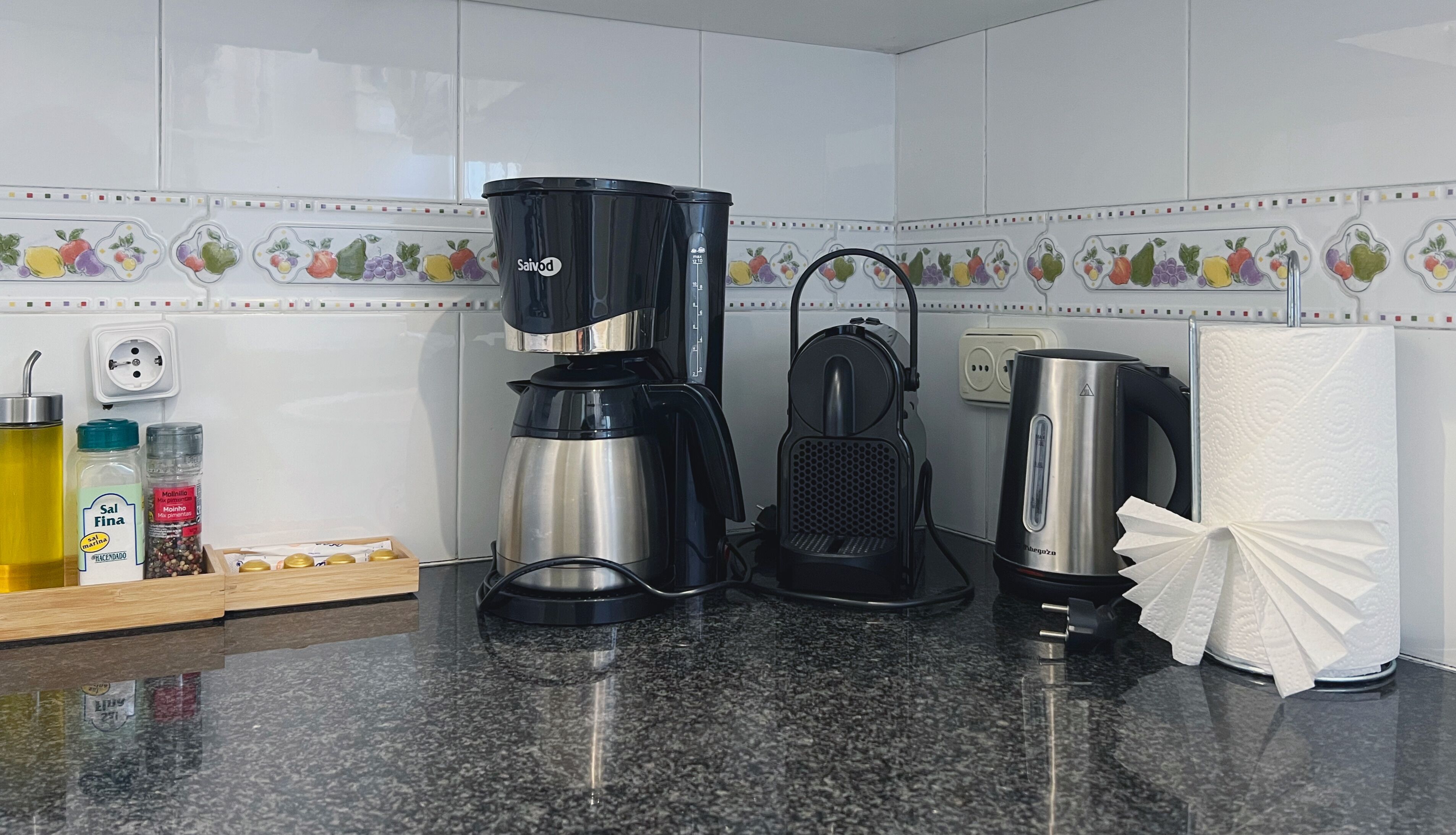 A kitchen with a coffee maker, kettle, and a box of coffee pods on the counter.