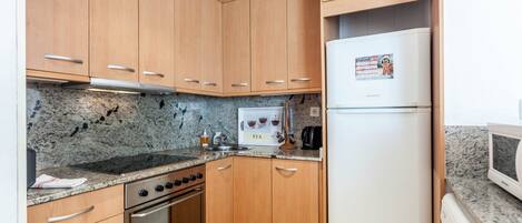 A compact kitchen with wooden cabinets, a built-in oven, a microwave, and a refrigerator.