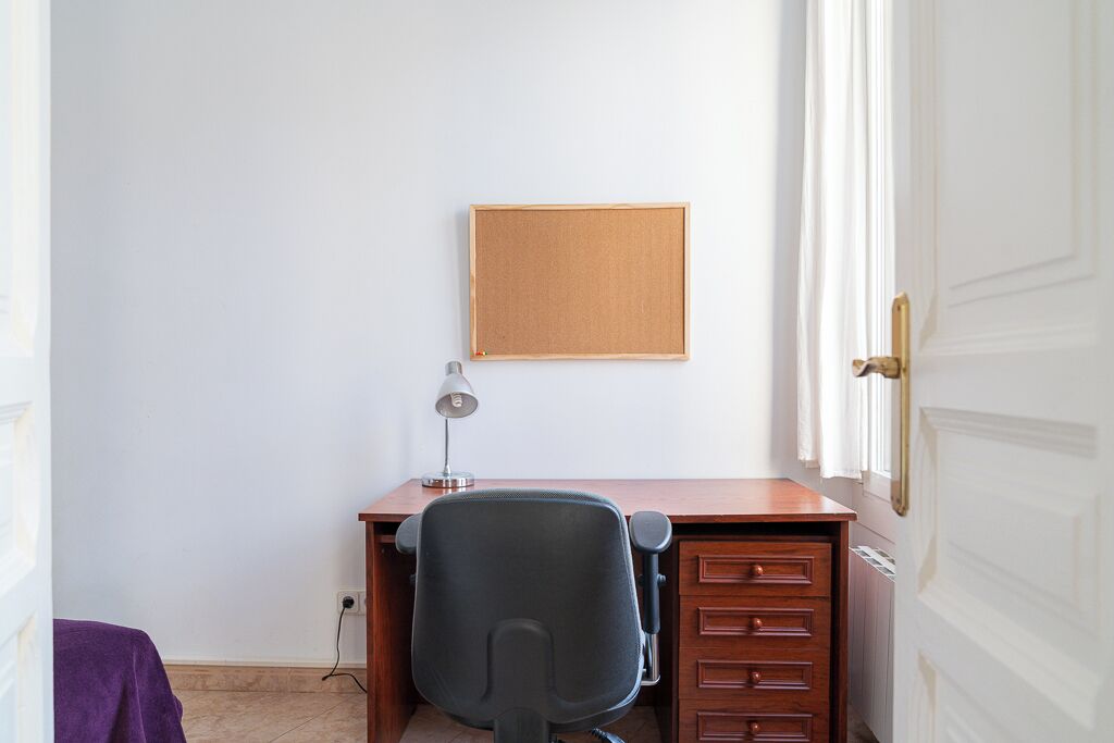 Ein kleiner Büroraum mit Schreibtisch, Stuhl und einer Pinnwand.