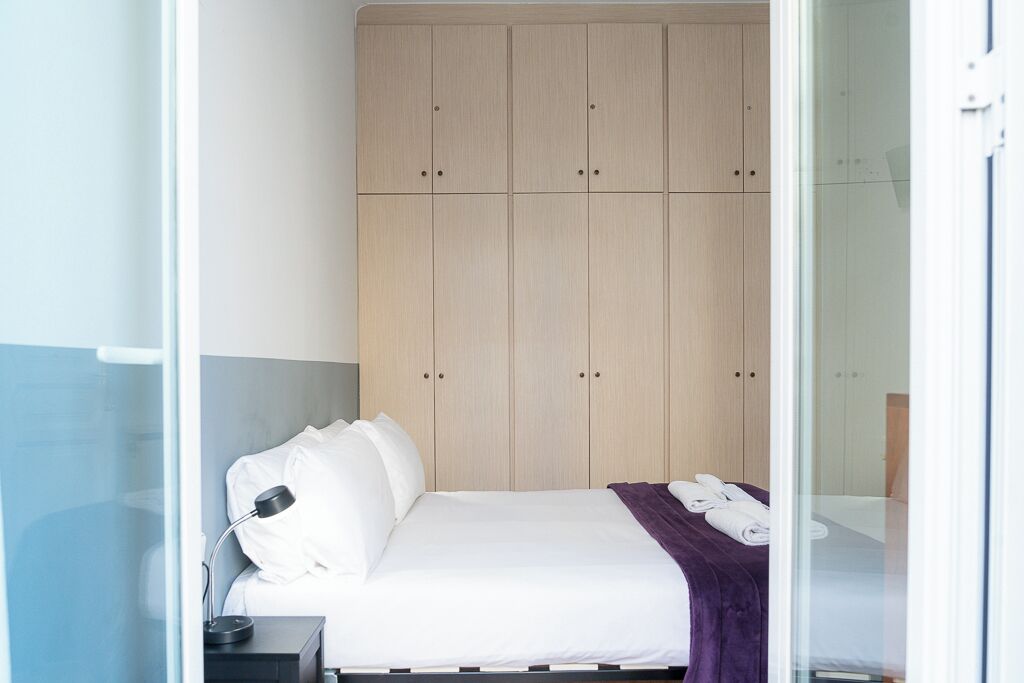 A hotel room with a bed, a nightstand, a lamp, and a wardrobe.