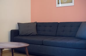 Un canapé bleu foncé avec un seul coussin, une petite table ronde en bois et un tableau encadré sur un mur de couleur pêche.
