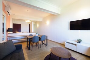 Ein modernes Wohnzimmer mit einer Couch, einem Esstisch mit Stühlen, einem Fernseher und einer schlichten weißen Kommode.