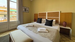 Une chambre d’hôtel avec un grand lit, une banquette, une table de chevet et une vue sur les bâtiments à l’extérieur de la fenêtre.