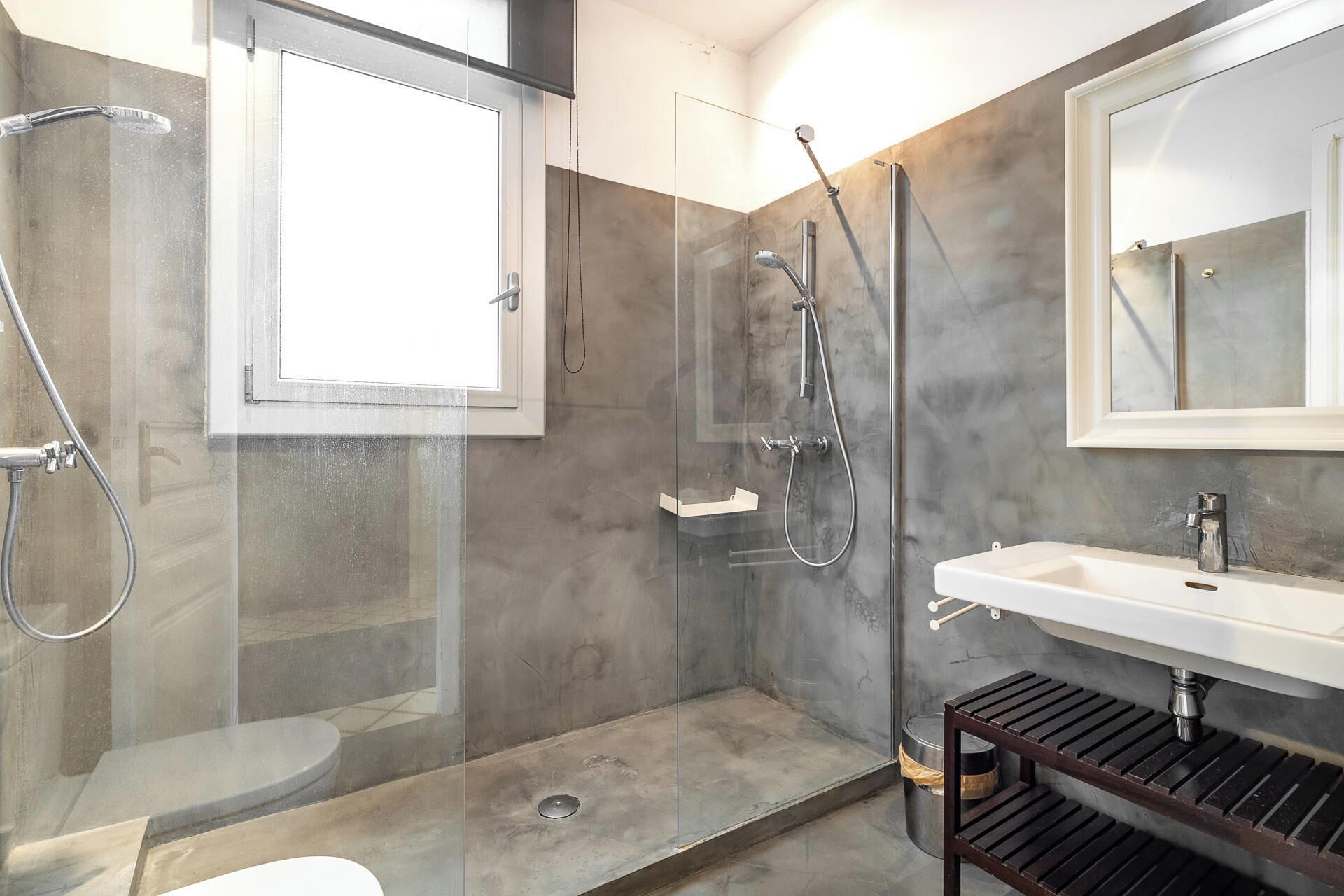 Une salle de bain moderne avec une douche à parois de verre, des toilettes et un lavabo doté d’une étagère en bois.