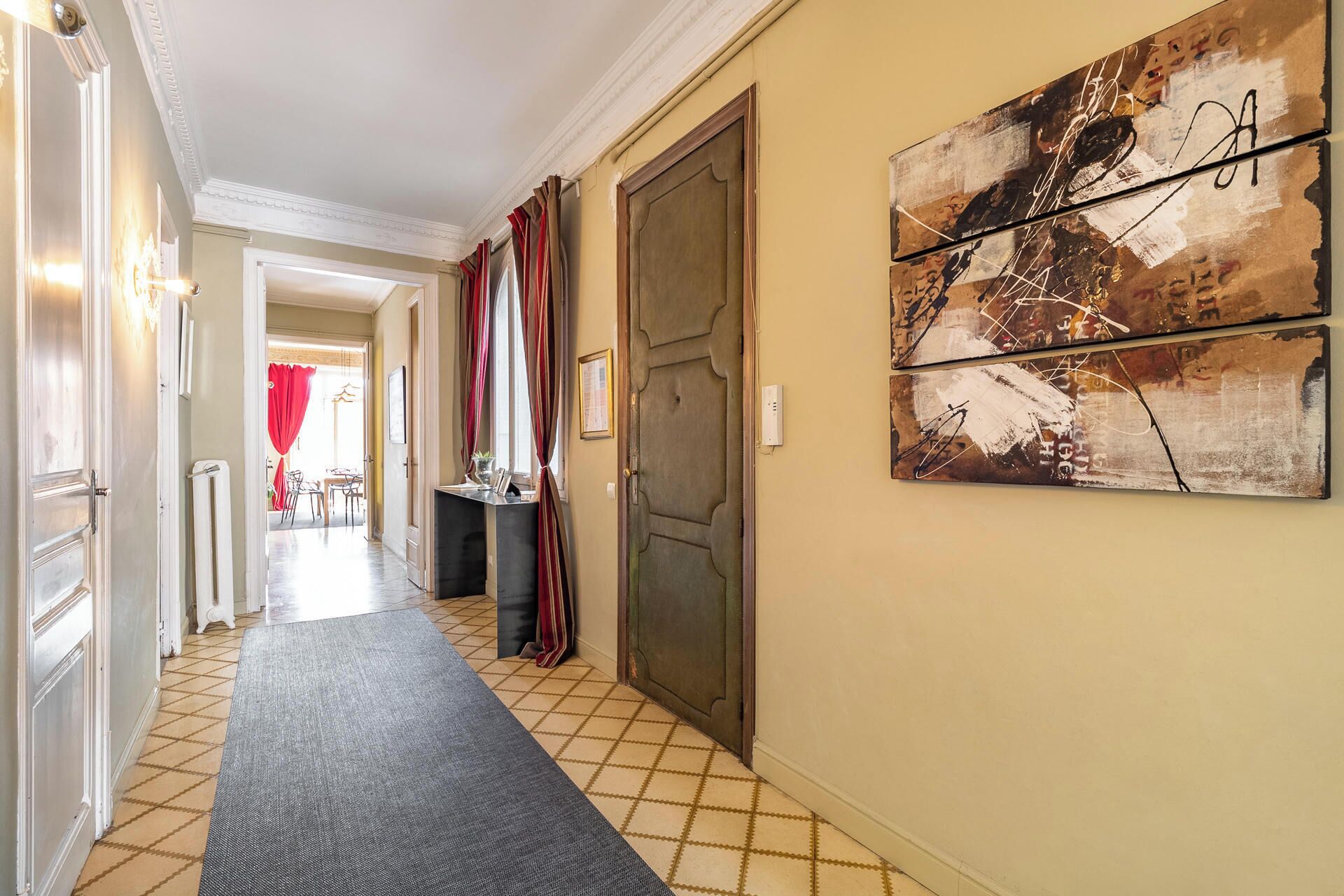 Un pasillo con alfombra estampada, una puerta y un cuadro abstracto colgado en la pared.
