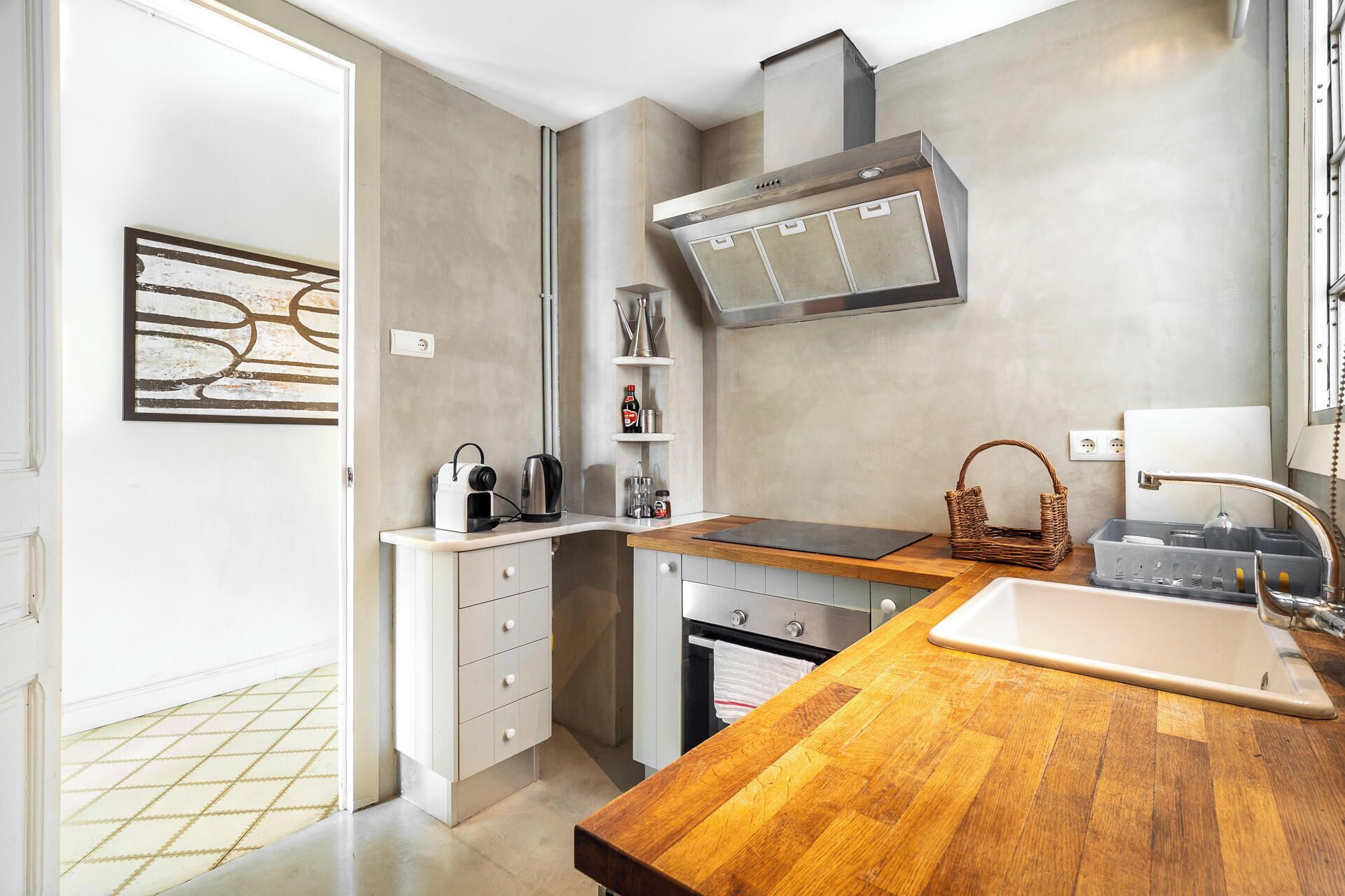 A compact kitchen with a wooden countertop, a stainless steel range hood, a built-in oven, and a small sink.
