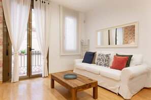 A living room with a white sofa, a wooden coffee table, and a balcony with white curtains. - Stay U-nique Apartments Terrassa (Barcelona)