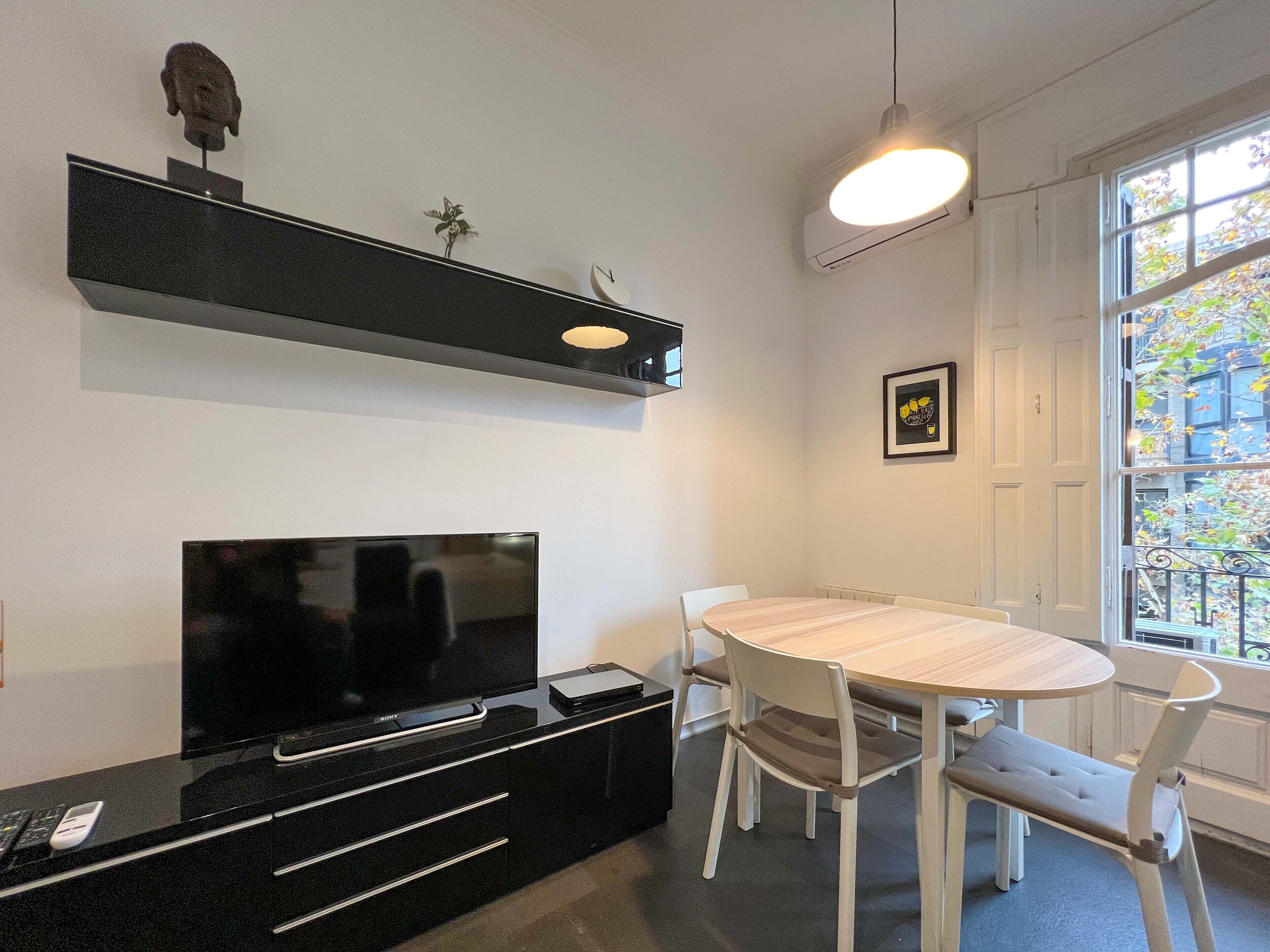 Een moderne woonkamer met een flatscreen televisie, een houten eettafel en witte stoelen.
