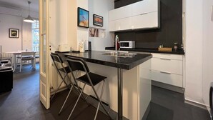 A modern kitchen with a black countertop, white cabinets, and a microwave. There are two black chairs at the bar counter. - Stay Unique Apartments Cent (Barcelona)
