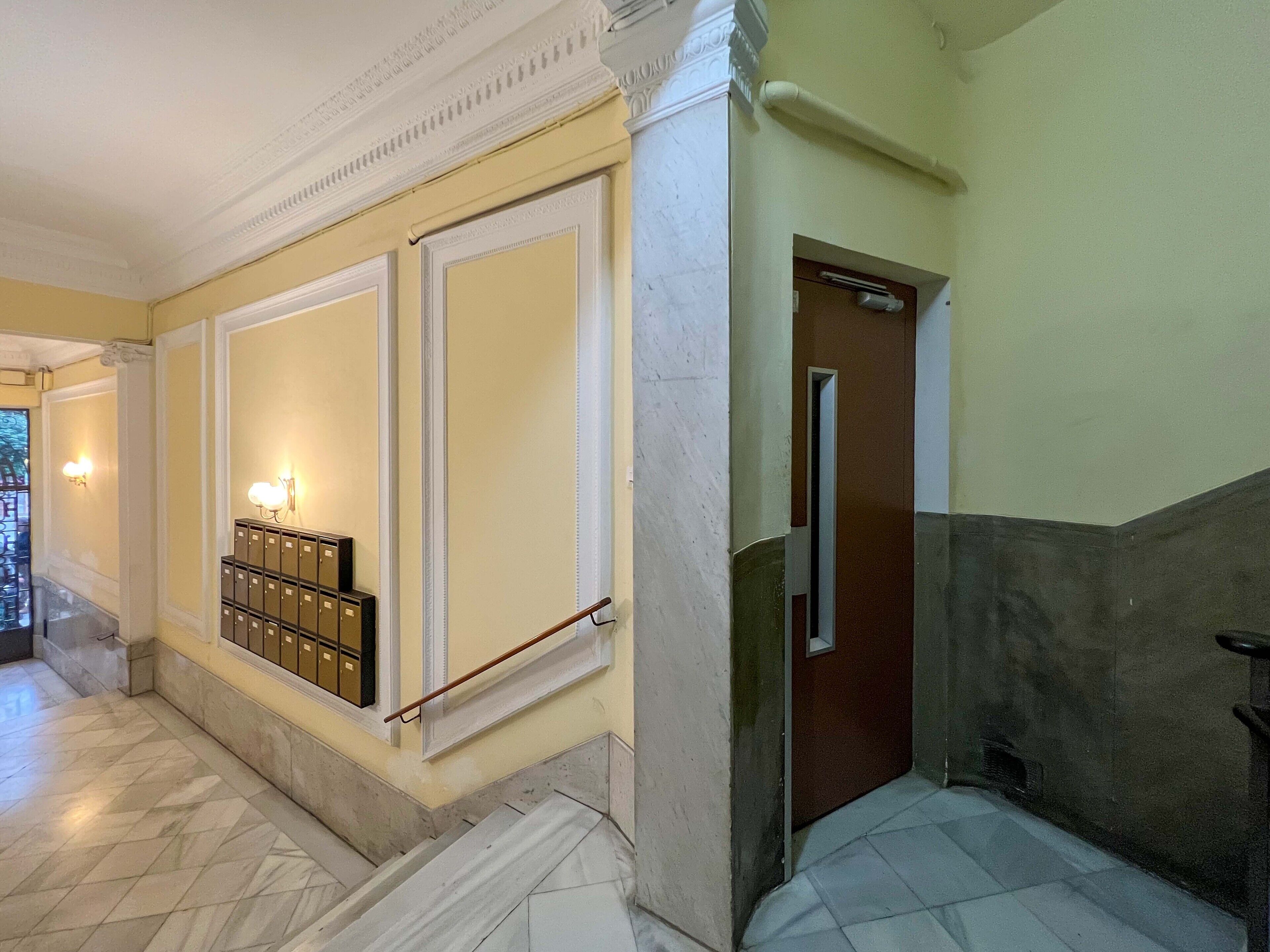 A hallway with a marble floor, a staircase, a door with a handle, and a wall-mounted light fixture.