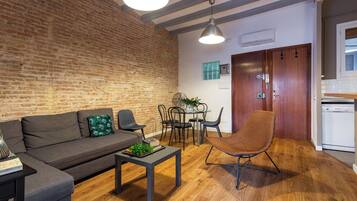 Una sala de estar moderna con pared de ladrillo, un sofá, una mesa de centro y una zona de comedor con sillas y una mesa.