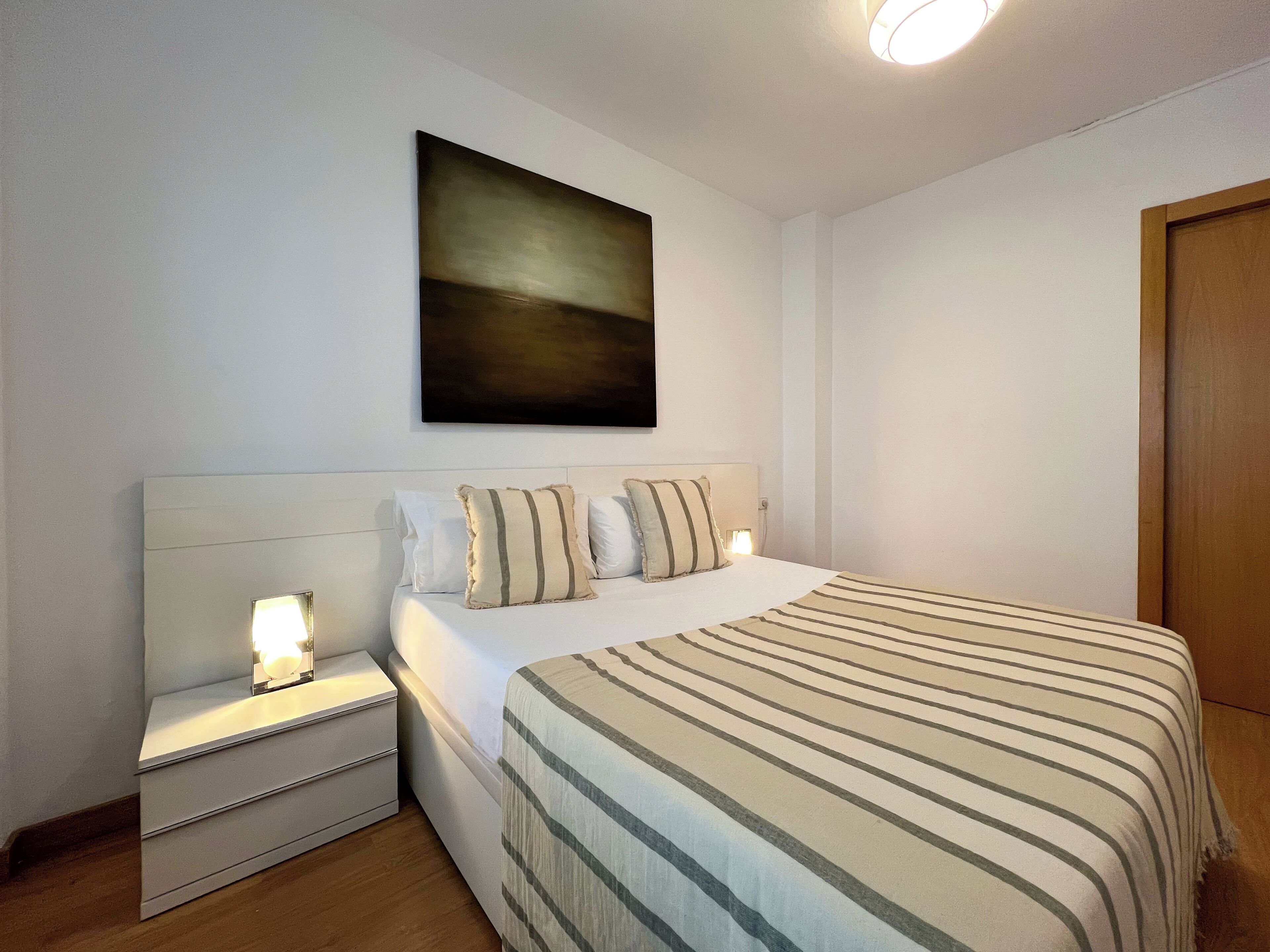 Un dormitorio con cama, mesitas de noche, una obra de arte colgada en la pared y una puerta de madera.